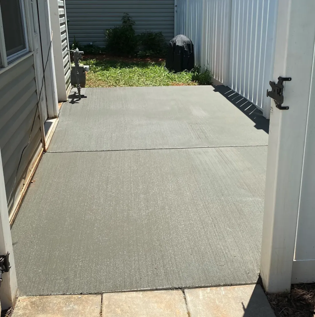 Small concrete patio beside a house and fence
